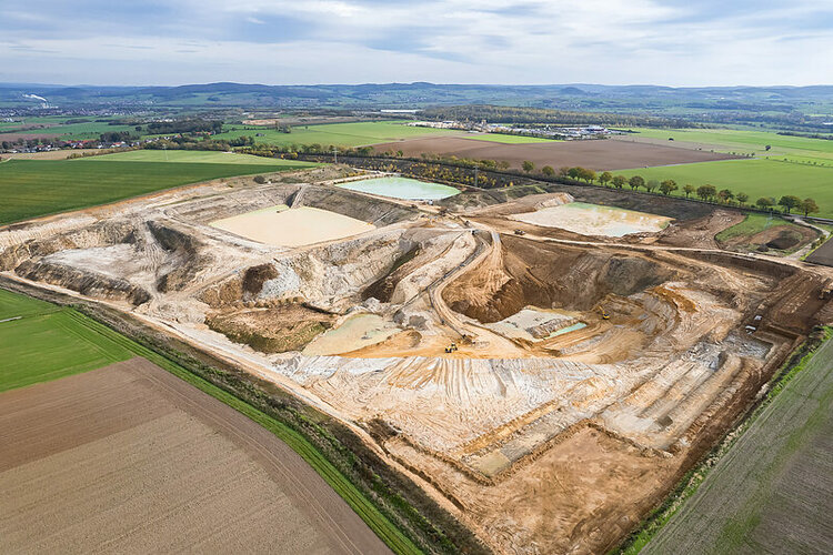 Vogelperspektive auf das Lehmabbaugebiet des Unternehmens Kimm-Baustoffe am Standort Hessen inmitten grüner Felder und flacher Landschaft